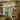 Model wearing pine green Promenade swing coat over a green floral tea dress with a yellow beret and blue handbag