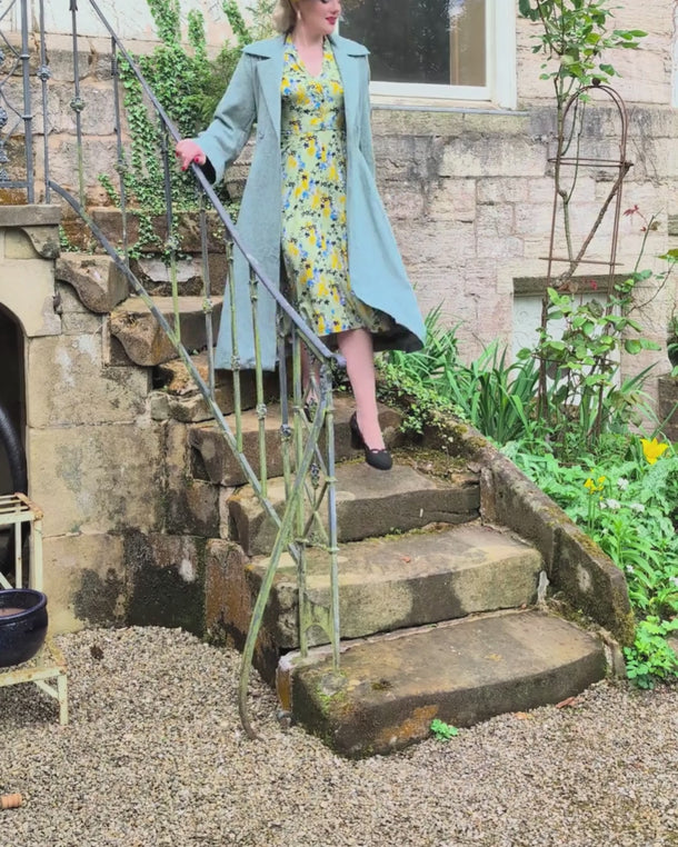 Model in a long vintage coat and floral dress walking down stone steps carrying a marine teal blue frame handbag